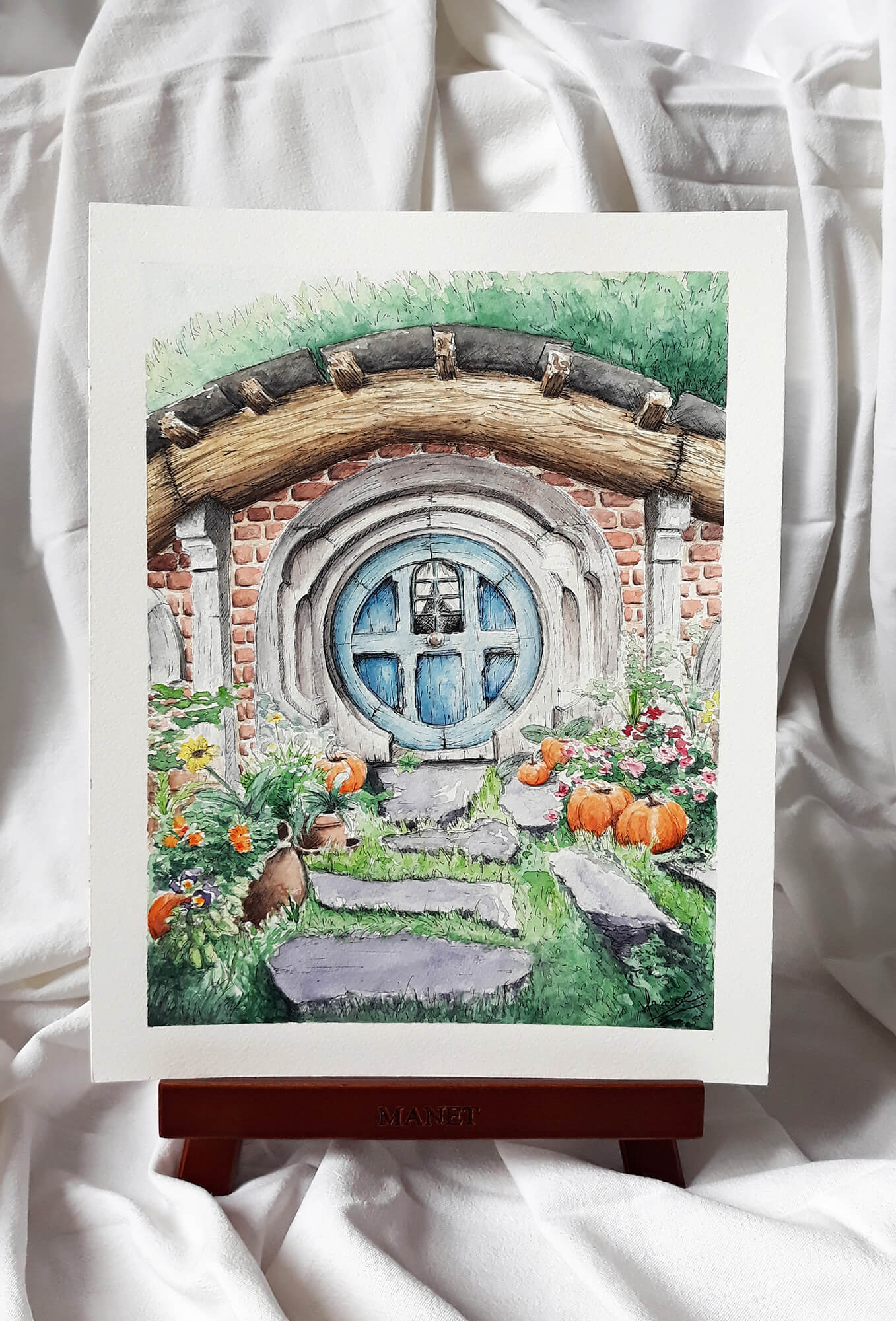 Aquarelle originale sur chevalet d'une façade de maison de Hobbit de la Comté avec sa porte ronde ©Hisae illustrations